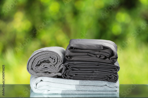 Stack of folded bedding. Monochrome gray gradient plaid towel bedsheet textile set on blurred foliage background