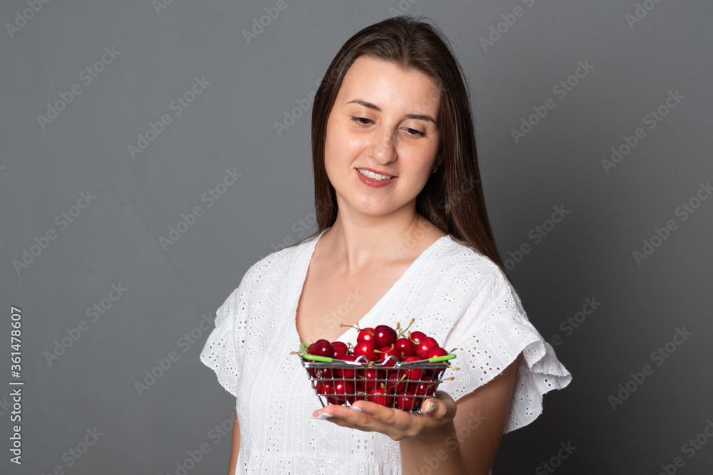 Positive woman holds a basket of cherries. Smiling girl in a summer dress holds a cherry. Positive woman holds a basket of cherries. Smiling girl in a summer dress holds a cherry.