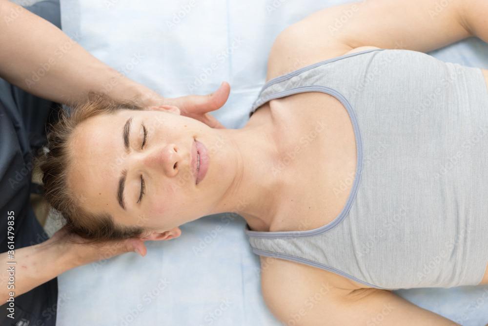 Young woman with closed eyes having a chiropractic treatment in the clinic - lying on the couch and the doctor holding her neck Young woman with closed eyes having a chiropractic treatment in the clinic - lying on the couch and the doctor holding her neck