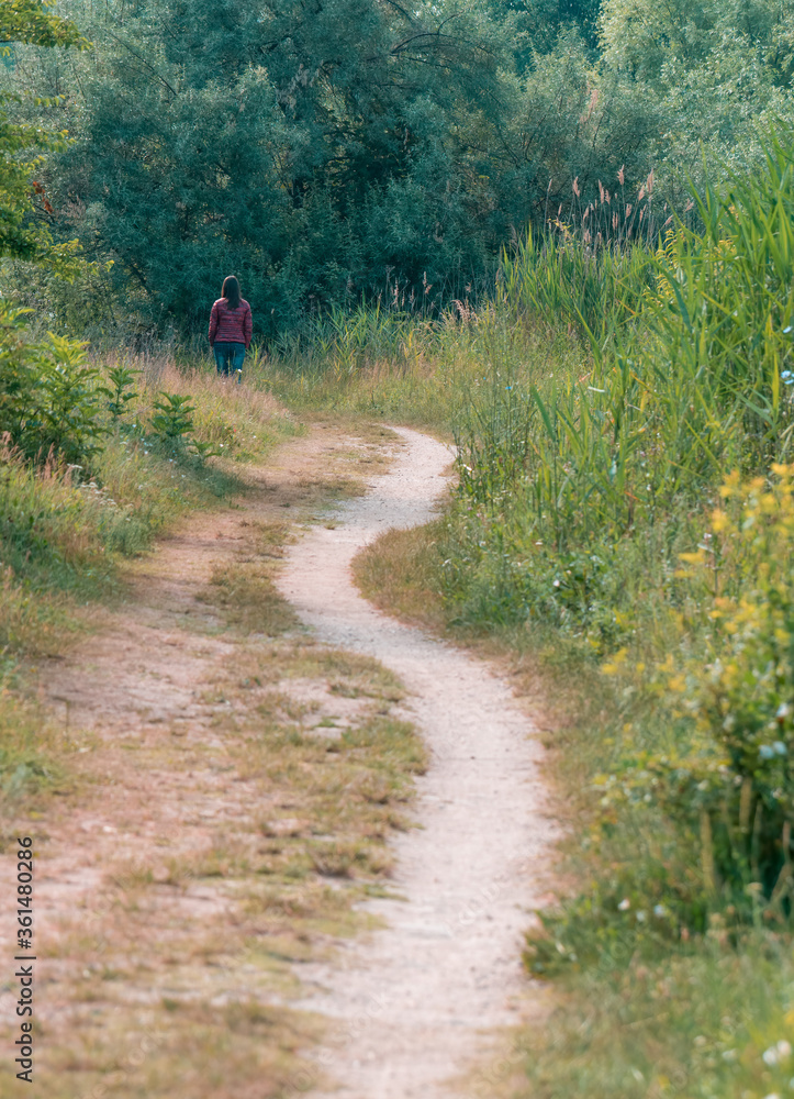 Lonely girl walking on a footpath surrounded by trees and high grass. Pathway in Vacaresti Park Nature Reserve. Lonely girl walking on a footpath surrounded by trees and high grass. Pathway in Vacaresti Park Nature Reserve.