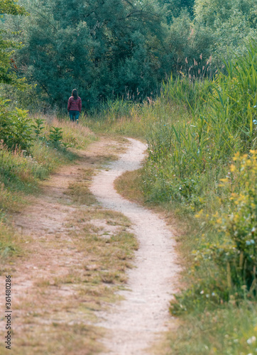 Lonely girl walking on a footpath surrounded by trees and high grass. Pathway in Vacaresti Park Nature Reserve. © Cristi