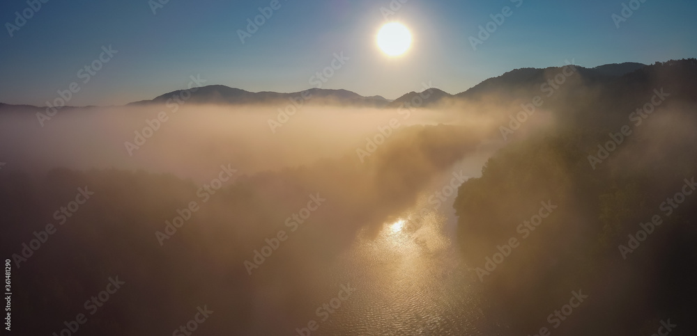 Aerial drone panorama of river and fog over misty plains with hills perking out of the fog during early sunrise hours. Early morning on river and fields.