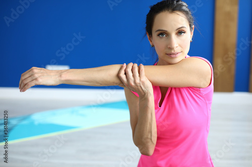Portrait of beautiful young woman training arm. Charming concentrated yoga instructor in class. Bright pink shirt for sport. Active lifestyle and health concept