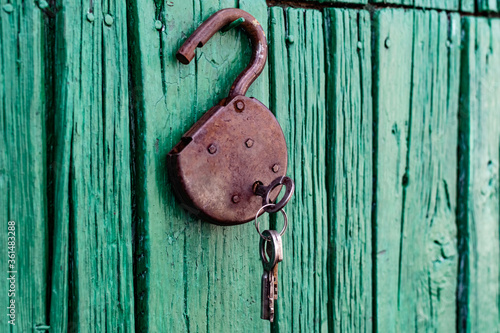 Old barn locks with keys hang on the painted green wood wall. Rusty metal device for closing doors.