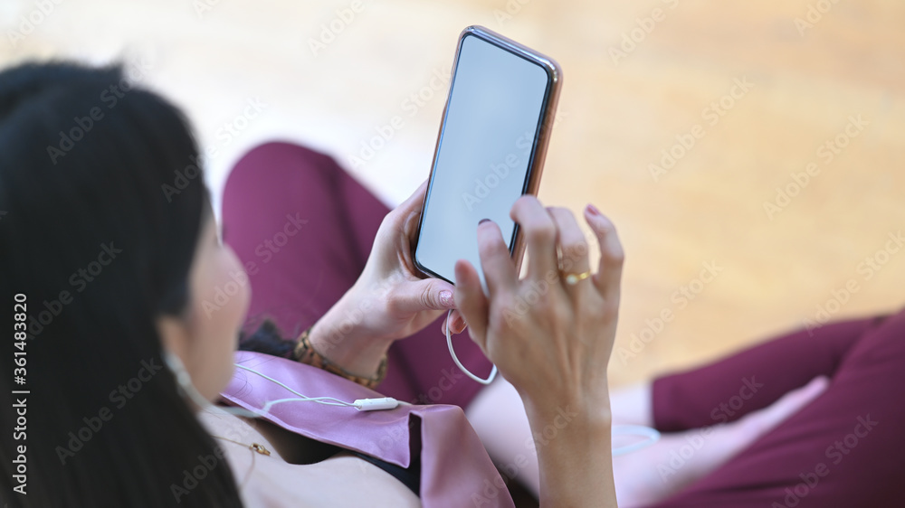 The top view image of a woman is relaxing with a white blank screen smartphone in the living room. The top view image of a woman is relaxing with a white blank screen smartphone in the living room.
