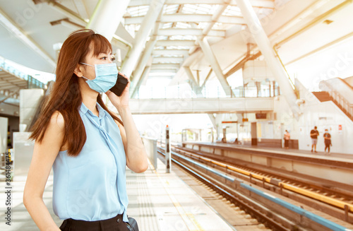 business woman wearing face mask at train station talking on the mobile phone © Tom Wang