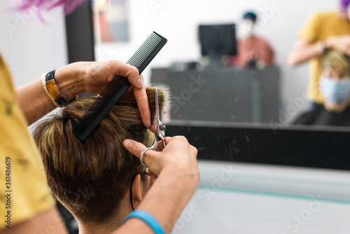 Concept: unconfinement after coronavirus, covid-19. Detail of professional hairdresser's hands. Cutting hair to brown short hair woman at hairdresser.
