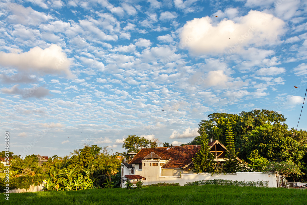 Blue sky with many little white clouds over the roofs of a village. Badung, Bali, Indonesia, Blue sky with many little white clouds over the roofs of a village. Badung, Bali, Indonesia,