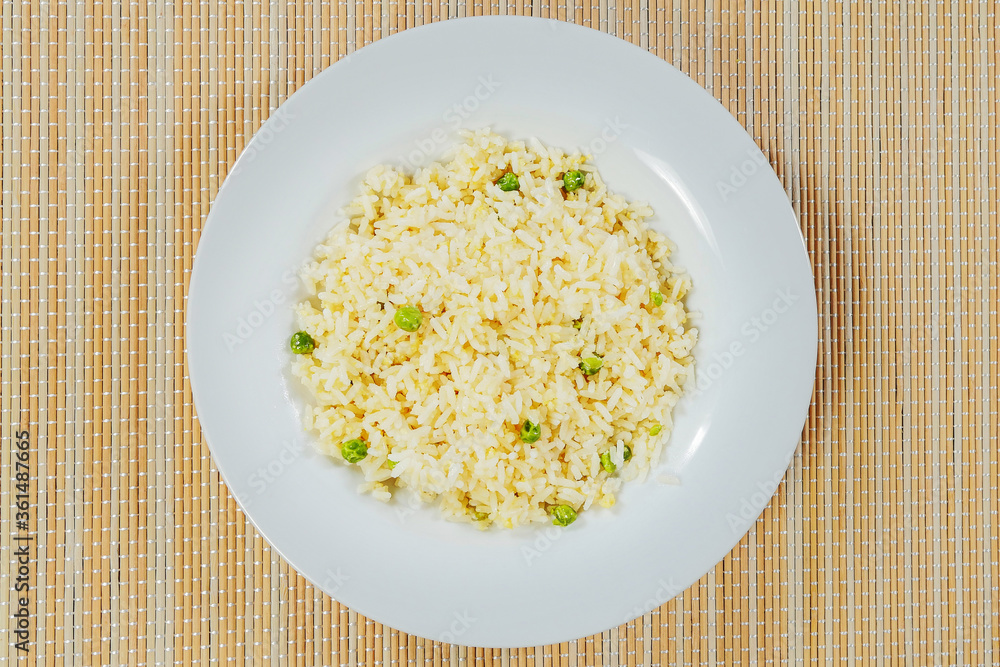 Cooked jasmine rice with green peas on a white plate and bamboo table