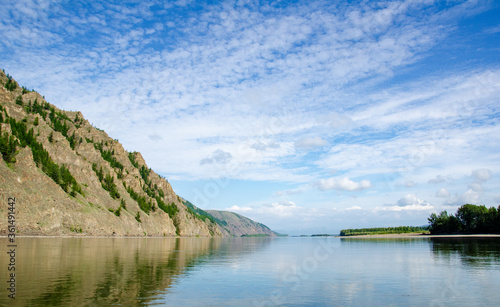 A clear Sunny summer day on the lake. A small mountain is reflected in the water surface. Green forest.