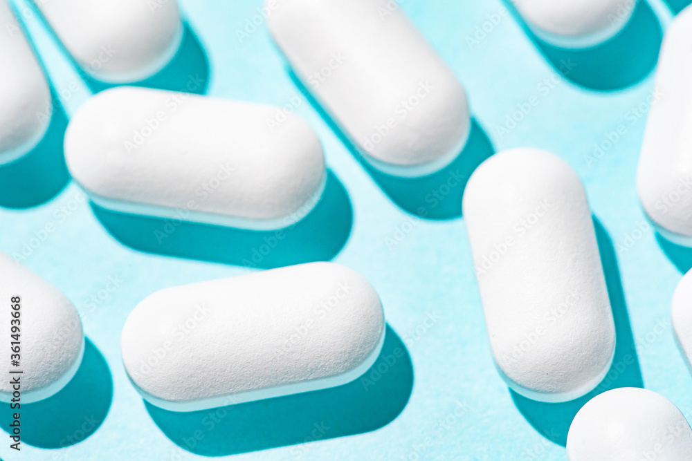 White tablets on a light pastel blue table. Repeated pills on a blue background. Macro White tablets on a light pastel blue table. Repeated pills on a blue background. Macro