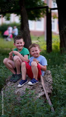 Two funny boys sitting on a large stone in the park.