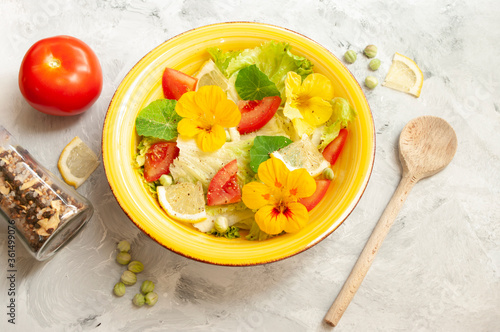 Fresh summer salad with edible flowers nasturtium, borage flowers in a yellow ceramic bowl. photo