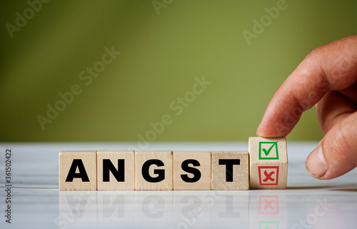 The hand turns the wooden cube and changes the german word ANGST (english = fear) with green positive tick check box and red reject X check box.