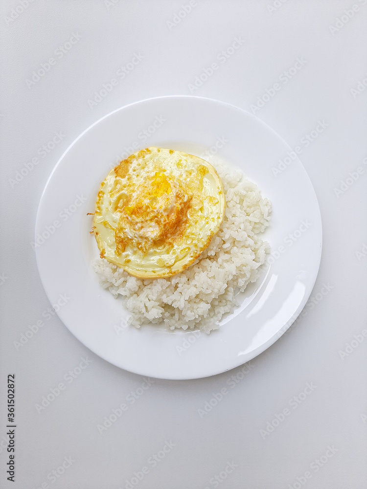 Fried egg or overcooked sunny side up, served with white rice, on a white plate, isolated in white background Fried egg or overcooked sunny side up, served with white rice, on a white plate, isolated in white background