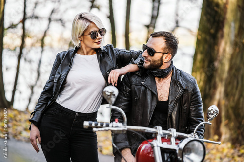 Pretty couple near red motorcycle on the road in the forest with colorful blured background