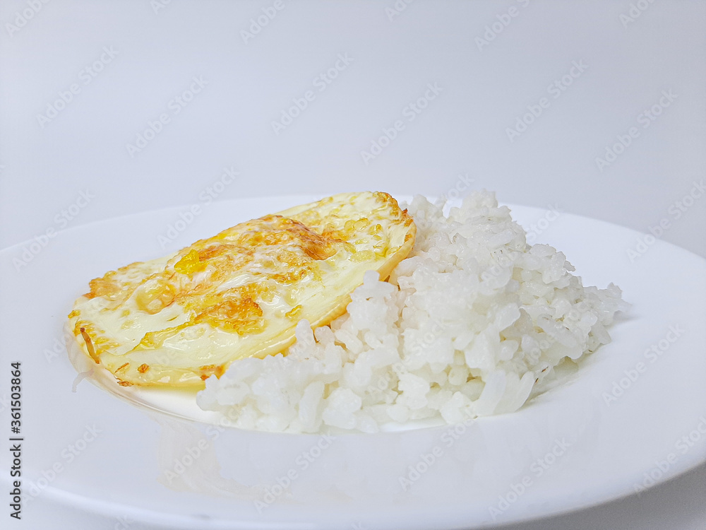 Fried egg or overcooked sunny side up, served with white rice, on a white plate, isolated in white background Fried egg or overcooked sunny side up, served with white rice, on a white plate, isolated in white background