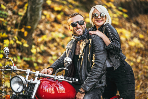 Pretty couple near red motorcycle on the road in the forest with colorful blured background