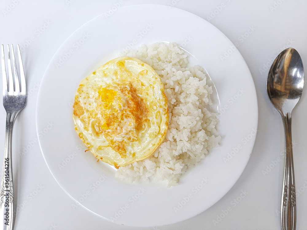 Fried egg or overcooked sunny side up, served with white rice, on a white plate, isolated in white background. Flat lay or top view or overhead