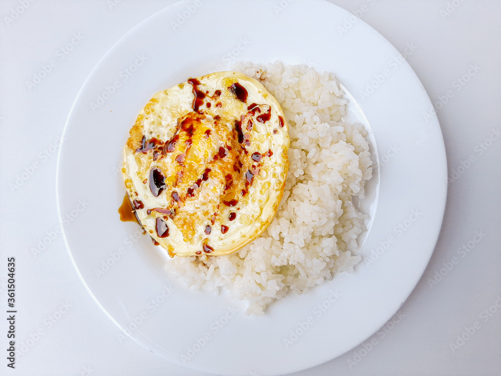 Fried egg or sunny side up, served with white rice and soy sauce, on a white plate, isolated in white background. Space for text