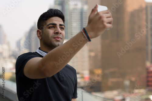 Young handsome Indian man taking selfie in the city