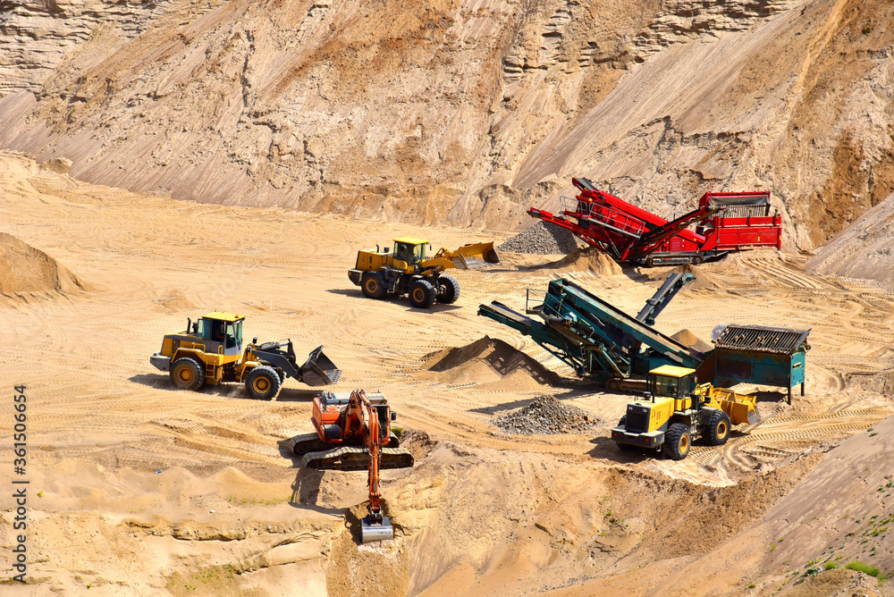Wheel front-end loader loads sand into a dump truck. Heavy machinery in the mining quarry, excavators and trucks. Mobile jaw crusher plant with belt conveyor puts crushing and screening process