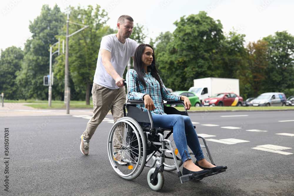 Portrait of couple walking on city street. Charming woman sitting in wheelchair. Caring man accompany female friend. Walking on fresh air. Disabled people concept