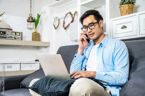Fotografija Asian businessman is sitting on the sofa in his own house taking a call on his m