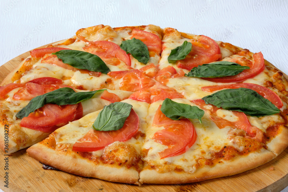 Pizza with tomatoes, basil and mozzarella on the wooden board. Delicious Italian food. Cafe, pizzeria and restaurant menu. Pizza with tomatoes, basil and mozzarella on the wooden board. Delicious Italian food. Cafe, pizzeria and restaurant menu.