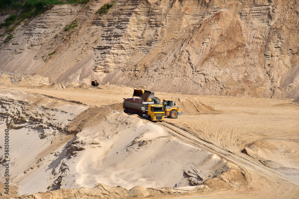 Wheel front-end loader loading sand into heavy dump truck at the opencast mining quarry. Dump truck transports sand in open pit mine. Quarry in which sand and gravel is excavated from the ground. Wheel front-end loader loading sand into heavy dump truck at the opencast mining quarry. Dump truck transports sand in open pit mine. Quarry in which sand and gravel is excavated from the ground.