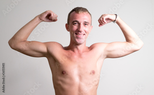 Portrait of happy man with blond hair flexing both arms shirtless