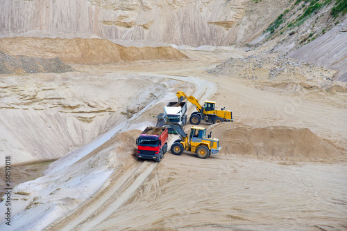 Wheel front-end loader loading sand into heavy dump truck at the opencast mining quarry. Dump truck transports sand in open pit mine. Quarry in which sand and gravel is excavated from the ground.