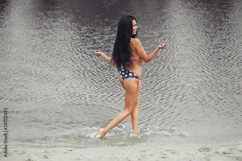 Fototapeta Naklejka Na Ścianę i Meble -  Young beautiful woman with beautiful body with american flag on the beach