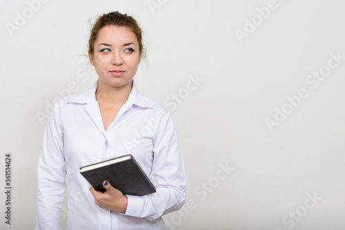 Portrait of young beautiful businesswoman thinking while holding book