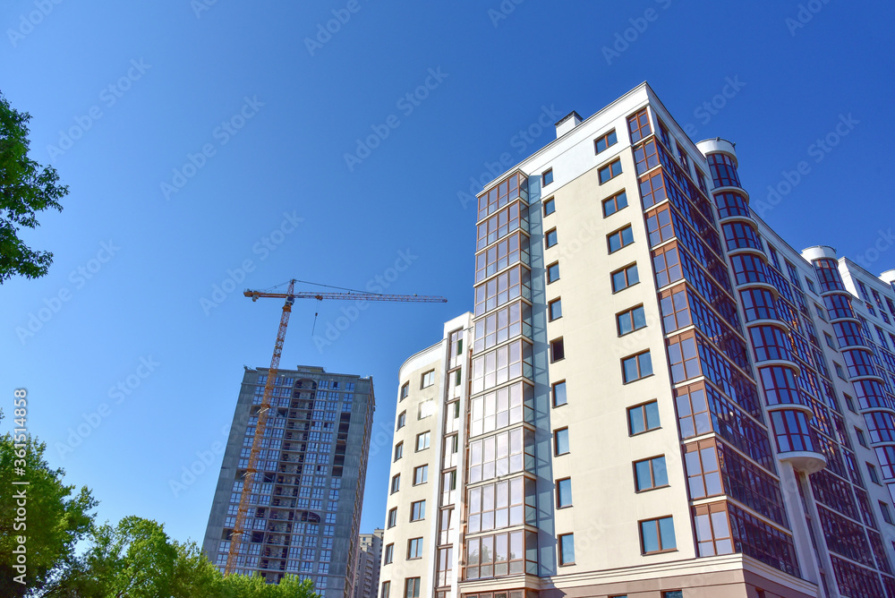 Tower cranes working at construction site on blue sky background. Construction process of the new modern residential buildings. Installing double glazed windows in building