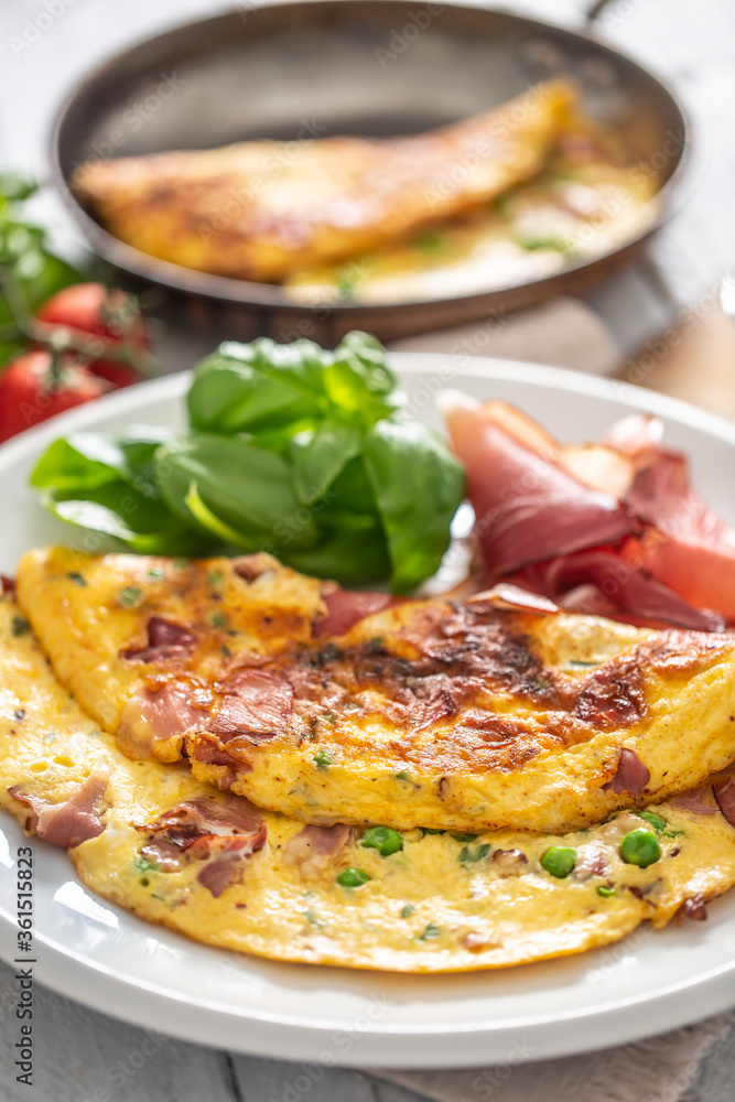 Omelette with prosciutto peas basil tomatoes and herbs on white plate Omelette with prosciutto peas basil tomatoes and herbs on white plate