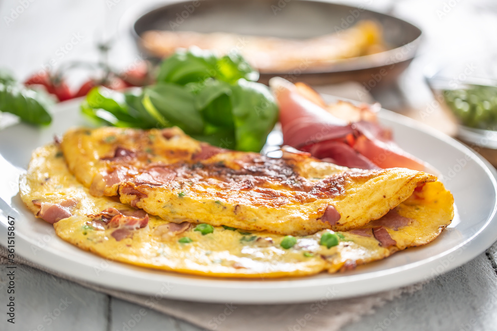 Omelette with prosciutto peas basil tomatoes and herbs on white plate Omelette with prosciutto peas basil tomatoes and herbs on white plate