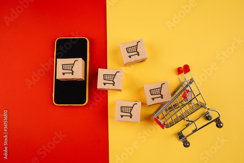 Paper brown boxes on smartphone and trolley isolate on colorful background. The concept of delivery of goods from the online store to the house.
