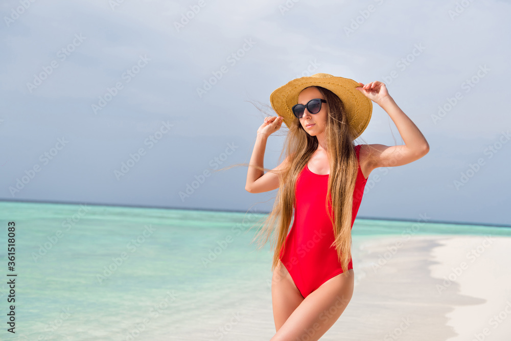 Photo of attractive tender lady long hairdo sunbathing stand sand sensual figure shapes seaside exotic resort wear sun headwear red bodysuit enjoy warm sun rays ocean beach outside