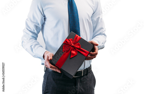 Business man holding a gift with a red ribbon. Guy on a white background in a light shirt with a tie. Black gift box in the hands..