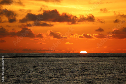 Sunset over the sea  orange sun is sinking in dramatic waves. Colorful sky with dark clouds  romantic background for travel and vacations