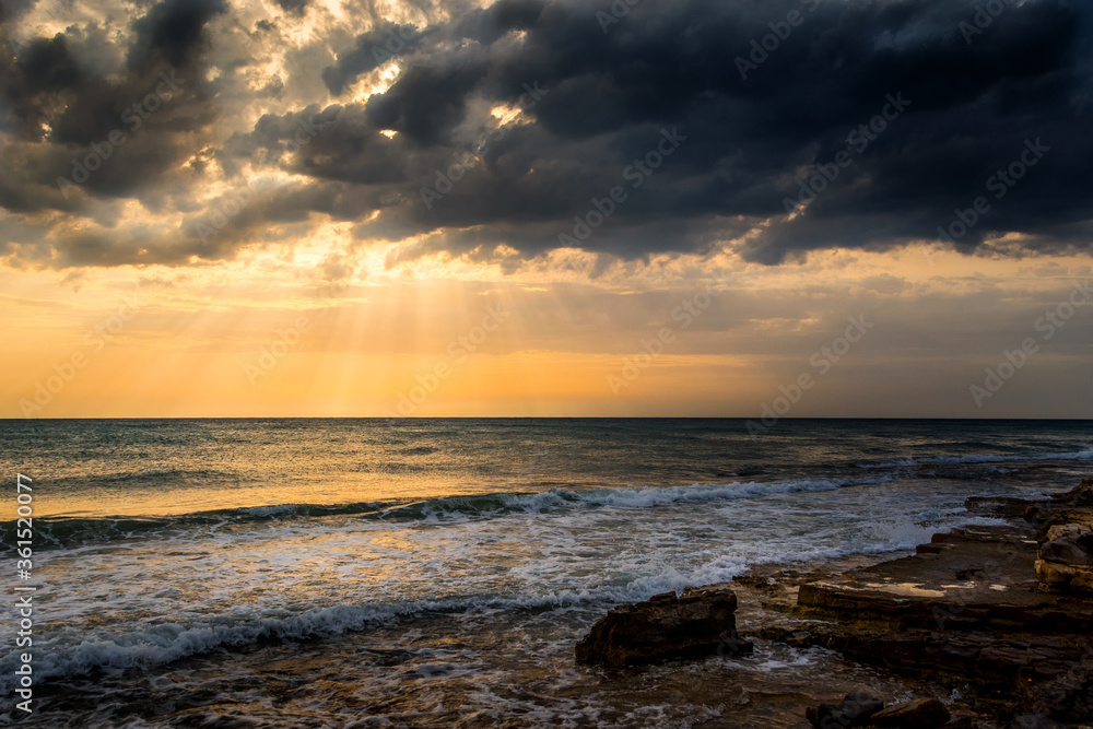 Calm sea waves hitting rocky seashore. Beautiful summer day with sunrays shining through clouds. Endless horizon over the ocean Calm sea waves hitting rocky seashore. Beautiful summer day with sunrays shining through clouds. Endless horizon over the ocean