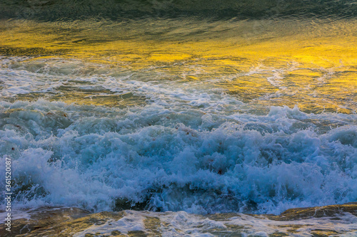 Sea waves hitting seashore at sunset. Yellow golden color reflected on surface. Close up view