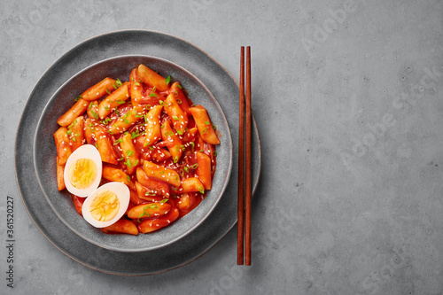 Tteokbokki with eggs in gray bowl on concrete table top. Tteok-bokki is a korean cuisine dish with rice cakes. Asian food. Top view. Copy space photo