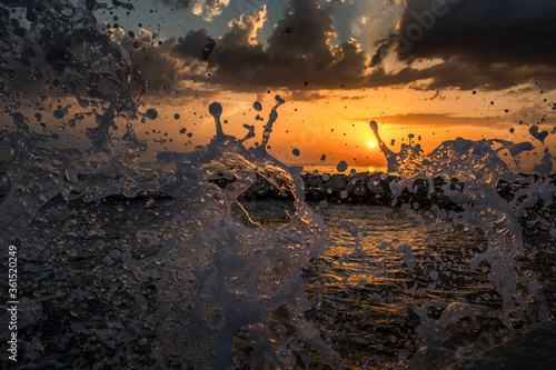 The waves breaking on a stony beach after summer storm. Water splash high in the air. Beautiful colorful orange sunset. Vacation at the sea. Wide angle, fast shutter speed