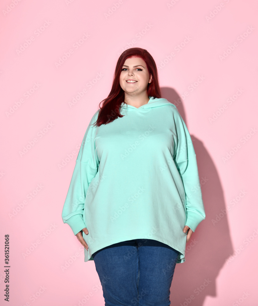 Charming plus-size model with long red hair and adorable smile posing calmly and confidently. Three quarter length shot isolated on pink Charming plus-size model with long red hair and adorable smile posing calmly and confidently. Three quarter length shot isolated on pink