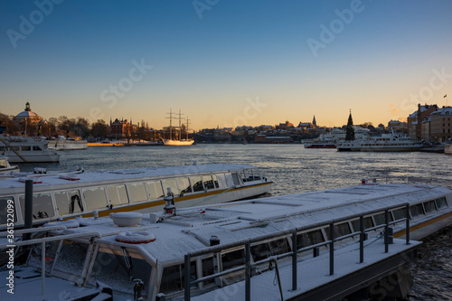 Snow covered water taxis docked along a harbor in Stockholm, Sweden during a winter sunset.