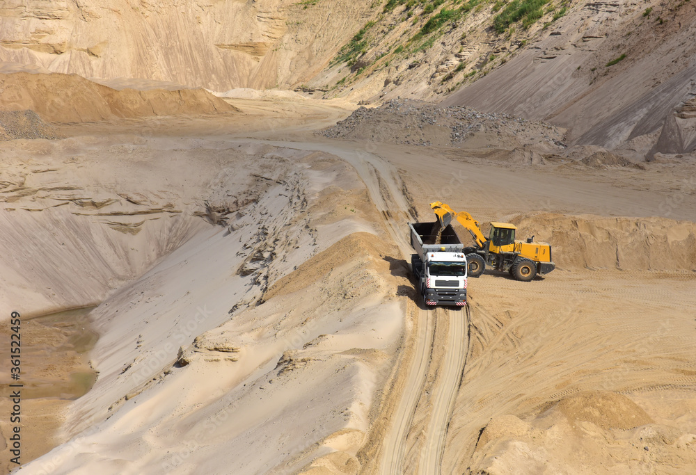 Wheel front-end loader loading sand into heavy dump truck at the opencast mining quarry. Dump truck transports sand in open pit mine. Quarry in which sand and gravel is excavated from the ground. Wheel front-end loader loading sand into heavy dump truck at the opencast mining quarry. Dump truck transports sand in open pit mine. Quarry in which sand and gravel is excavated from the ground.