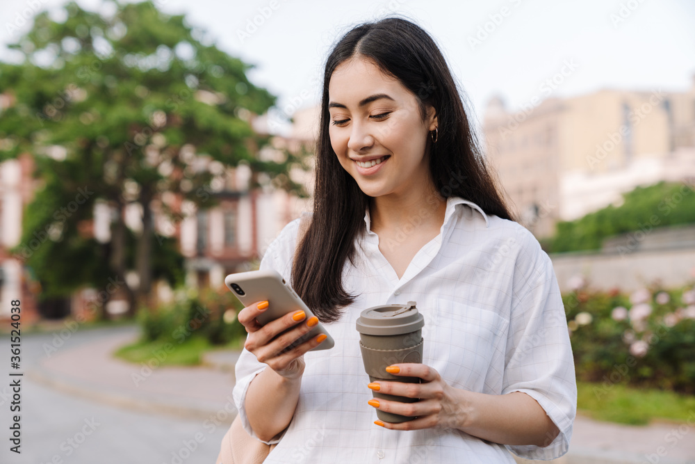 Photo of happy asian woman using cellphone and drinking coffee takeaway Photo of happy asian woman using cellphone and drinking coffee takeaway