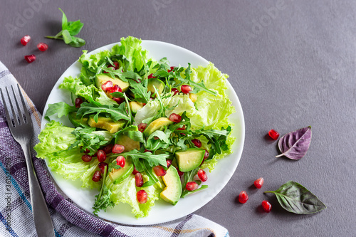Avocado and pomegranate salad on a white plate on a gray background.